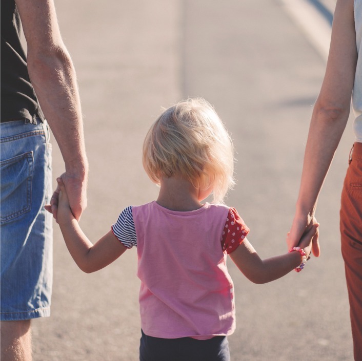 Mother and father walking away from camera while holding the hand of their child