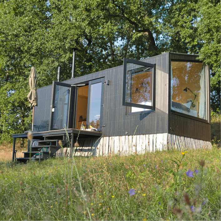 A tiny brown home sitting on the top of a grassy hill with trees