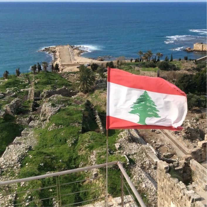 Flag of Lebanon waving with a cityscape and ocean scene in the background.