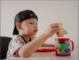 Young boy wearing a baseball cap sitting at a table with a sandwich