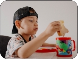 Young boy wearing a baseball cap sitting at a table with a sandwich